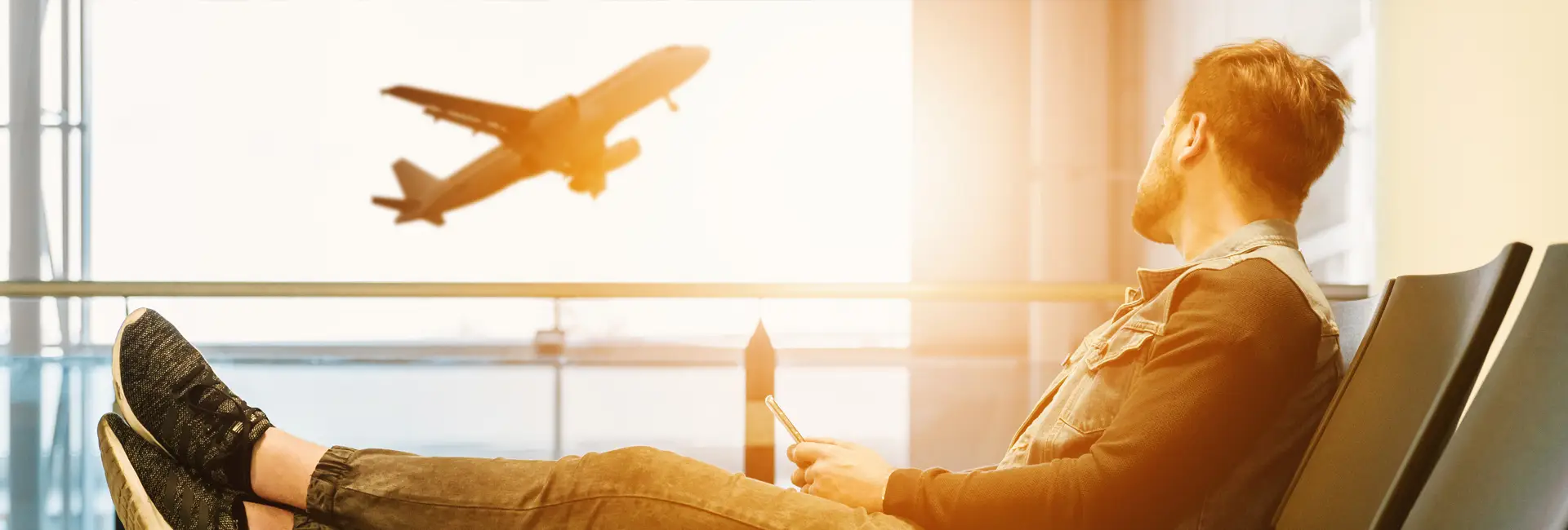 A traveller waiting at an airport window as a plane takes off